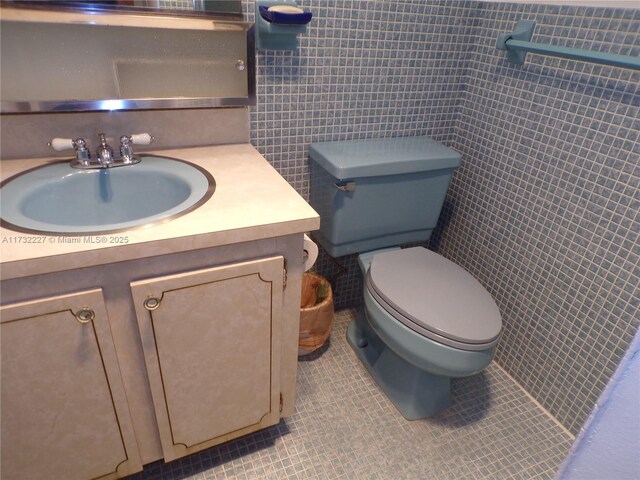 bathroom featuring tile patterned flooring, vanity, toilet, and tile walls