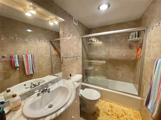 full bathroom with vanity, combined bath / shower with glass door, a textured ceiling, and toilet