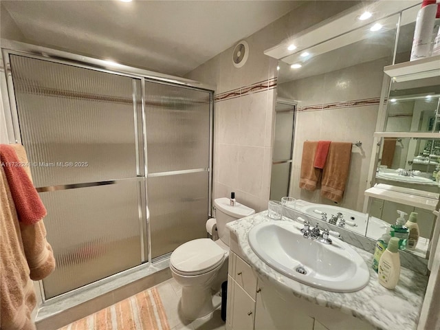 bathroom featuring tile walls, vanity, a shower with door, and toilet