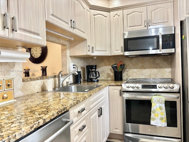 kitchen with light stone counters, sink, decorative backsplash, and appliances with stainless steel finishes