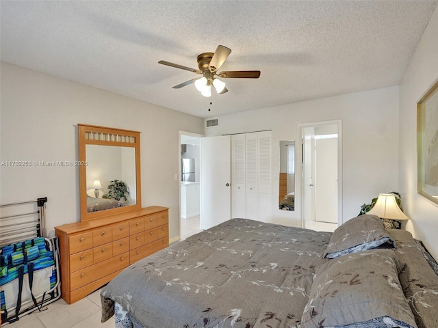 bedroom with stainless steel refrigerator, ceiling fan, a textured ceiling, light tile patterned flooring, and a closet