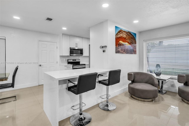 kitchen with stainless steel appliances, white cabinetry, a breakfast bar area, and light tile patterned floors