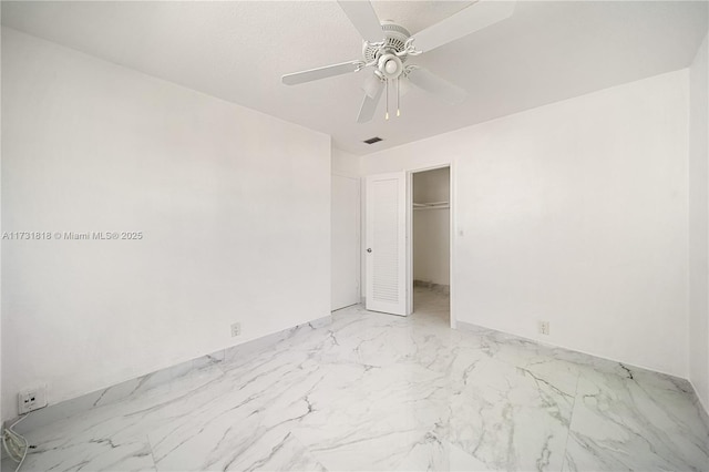 unfurnished bedroom with a textured ceiling, a walk in closet, a closet, and ceiling fan