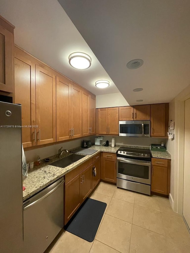 kitchen featuring light stone counters, sink, light tile patterned floors, and stainless steel appliances