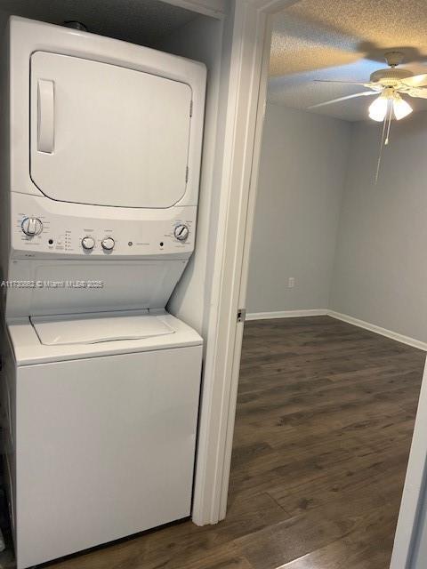 clothes washing area with dark wood-type flooring, ceiling fan, stacked washing maching and dryer, and a textured ceiling