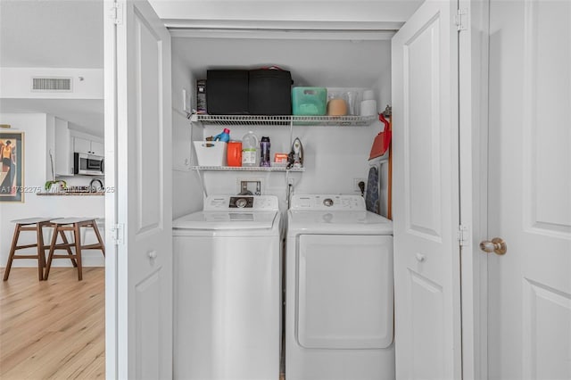 clothes washing area with washing machine and dryer and light hardwood / wood-style flooring