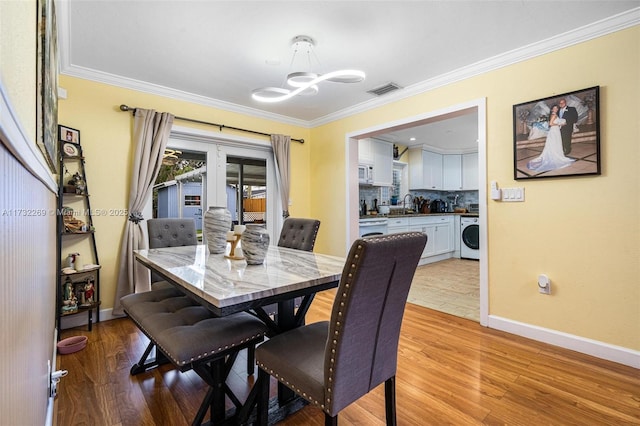 dining area with ornamental molding, light hardwood / wood-style floors, and washer / dryer