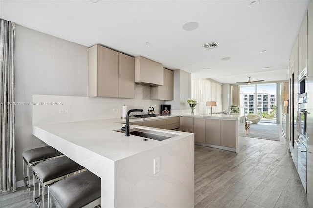 kitchen featuring sink, a breakfast bar, kitchen peninsula, oven, and light wood-type flooring