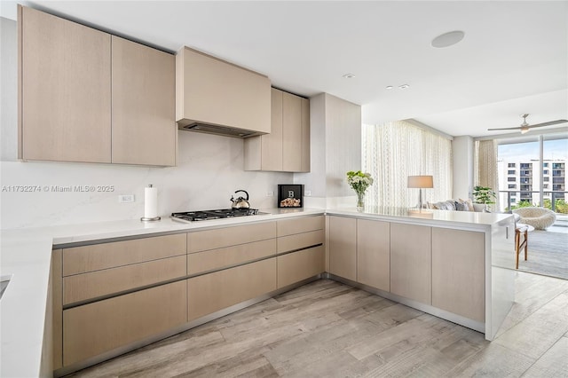 kitchen featuring stainless steel gas stovetop, light brown cabinetry, light wood-type flooring, and kitchen peninsula