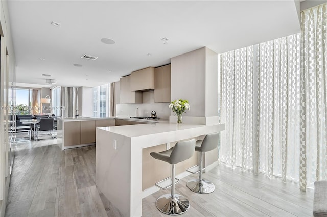 kitchen with a kitchen bar, light brown cabinets, kitchen peninsula, stainless steel gas stovetop, and light hardwood / wood-style floors