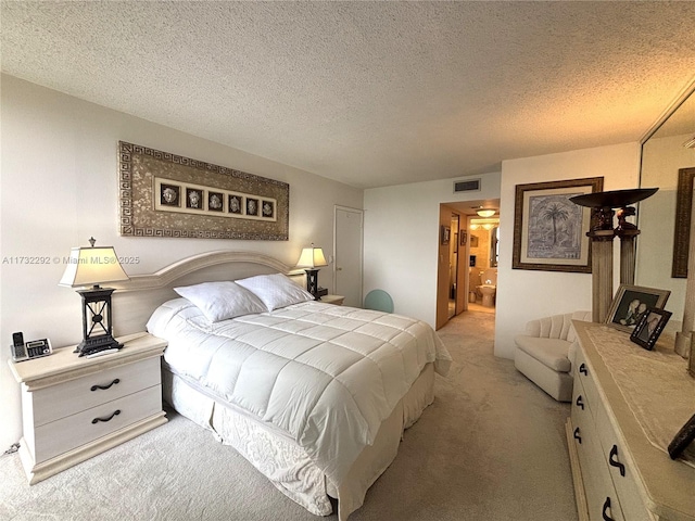 bedroom with light carpet, ensuite bath, and a textured ceiling