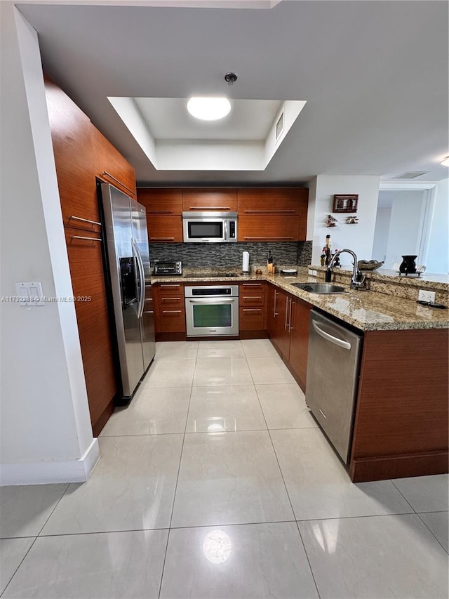 kitchen with a tray ceiling, light stone countertops, kitchen peninsula, and appliances with stainless steel finishes