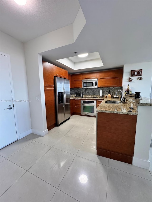 kitchen with sink, appliances with stainless steel finishes, kitchen peninsula, a raised ceiling, and light stone countertops