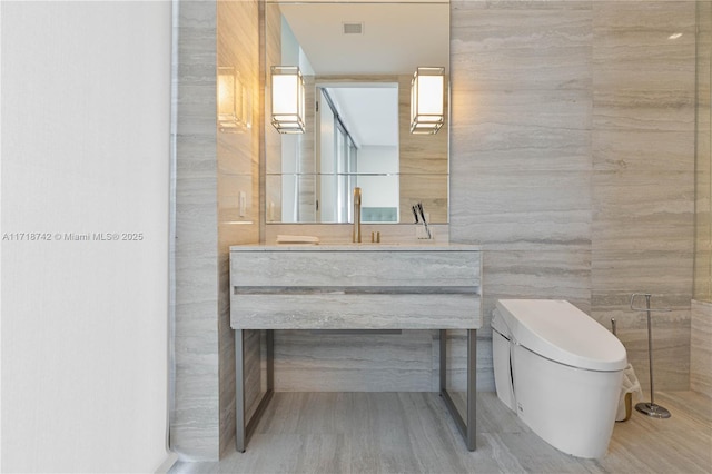 bathroom with vanity, tile walls, and toilet