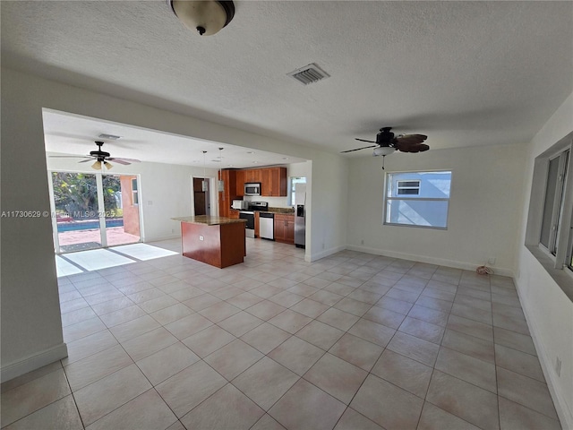 kitchen with ceiling fan, stainless steel appliances, a center island, a textured ceiling, and light tile patterned flooring