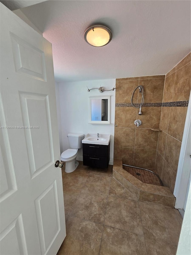 bathroom featuring vanity, a tile shower, tile patterned floors, and toilet