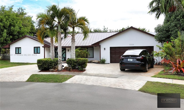 ranch-style home with metal roof, an attached garage, decorative driveway, stucco siding, and a standing seam roof