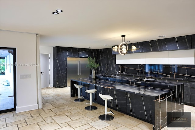 kitchen with a breakfast bar area, recessed lighting, stone tile flooring, stainless steel built in fridge, and a chandelier