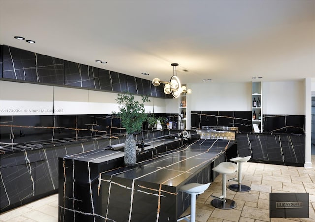 kitchen with tile walls, recessed lighting, stone tile flooring, hanging light fixtures, and a chandelier