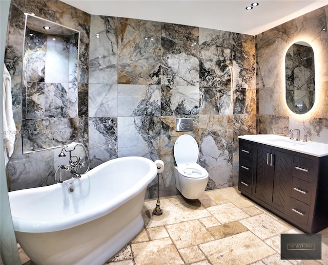 bathroom with stone tile floors, toilet, a freestanding bath, vanity, and tile walls