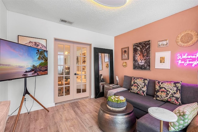 living room featuring light hardwood / wood-style flooring, french doors, and a textured ceiling