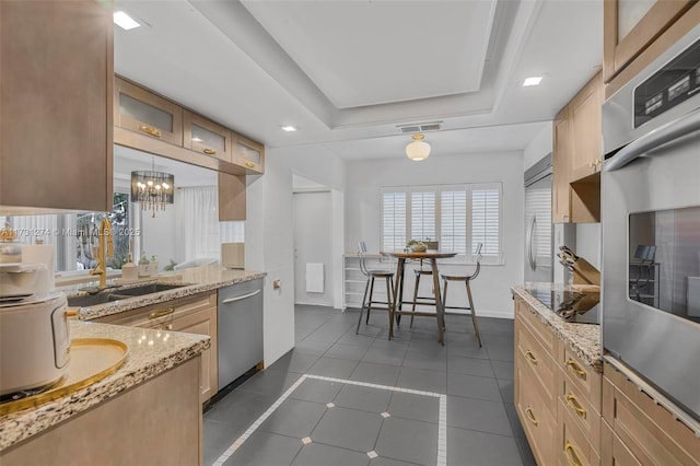 kitchen with hanging light fixtures, light brown cabinets, dark tile patterned flooring, a raised ceiling, and stainless steel appliances