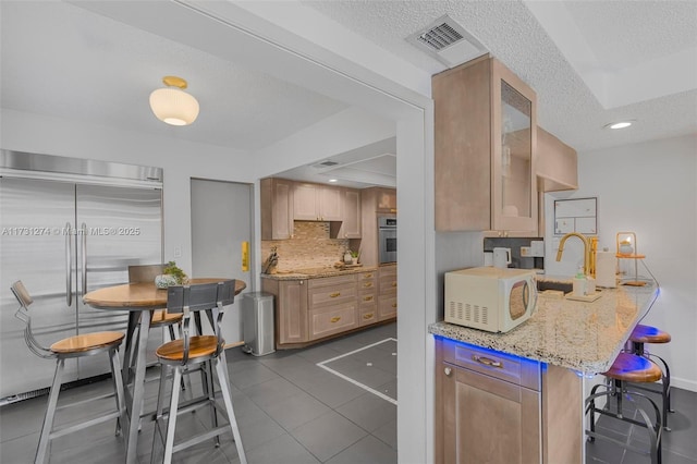 kitchen featuring light brown cabinetry, dark tile patterned flooring, light stone counters, and stainless steel appliances