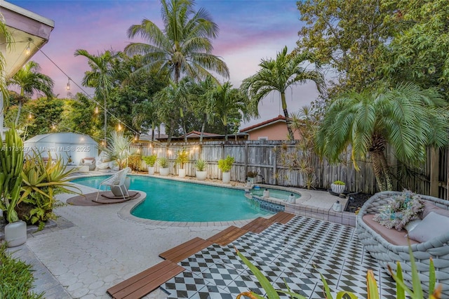 pool at dusk with a patio and an in ground hot tub