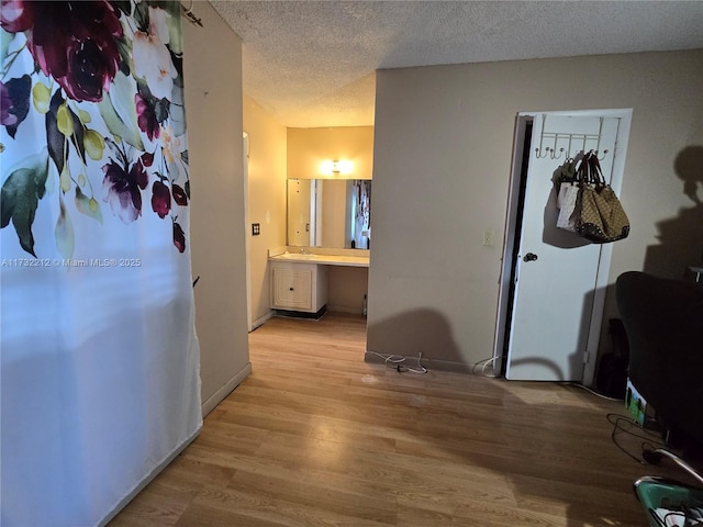 corridor with sink, a textured ceiling, and light wood-type flooring