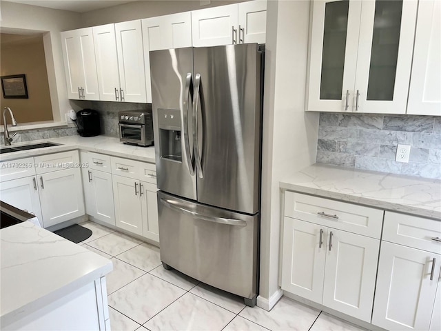 kitchen with white cabinetry, stainless steel fridge, sink, and light stone counters