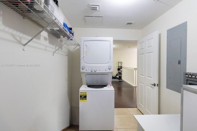 clothes washing area featuring light tile patterned flooring, stacked washing maching and dryer, and electric panel