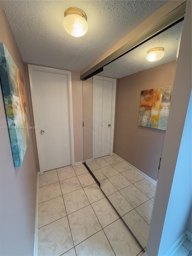 corridor with light tile patterned flooring, a textured ceiling, and baseboards