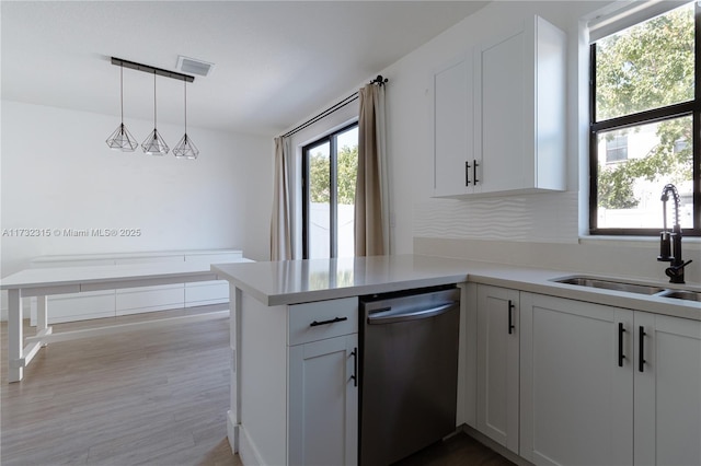 kitchen with sink, decorative light fixtures, stainless steel dishwasher, kitchen peninsula, and white cabinets