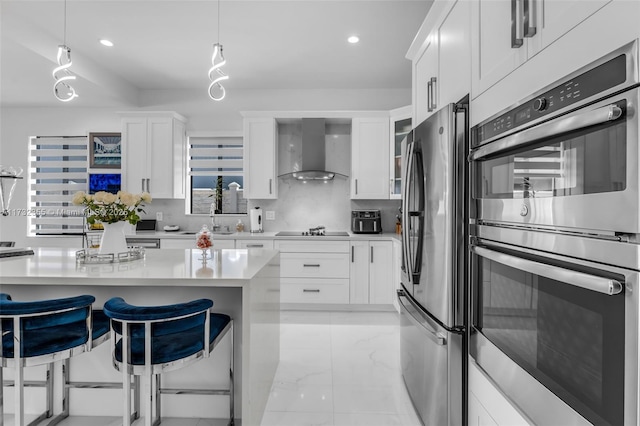 kitchen featuring white cabinetry, appliances with stainless steel finishes, a breakfast bar area, and wall chimney range hood