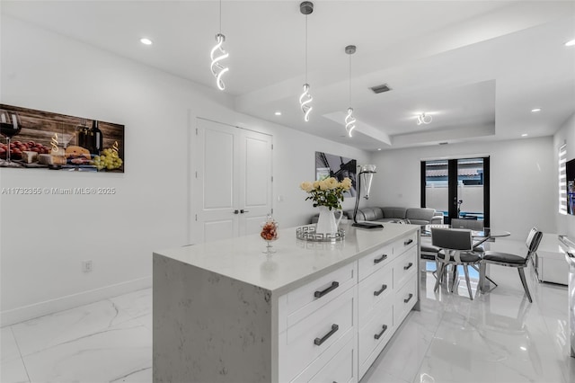 kitchen with white cabinets, hanging light fixtures, a center island, a raised ceiling, and light stone countertops