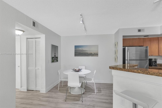 dining room featuring track lighting, a textured ceiling, and light hardwood / wood-style floors