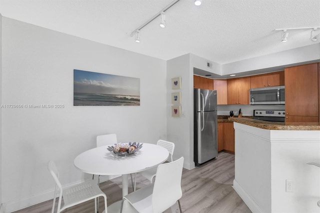 kitchen with appliances with stainless steel finishes, a textured ceiling, and light hardwood / wood-style floors