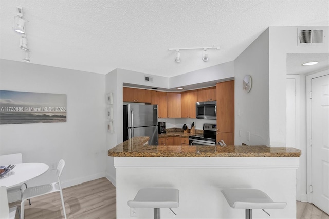 kitchen with stainless steel appliances, a breakfast bar, light hardwood / wood-style floors, and kitchen peninsula