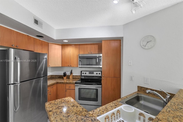 kitchen featuring appliances with stainless steel finishes, sink, a textured ceiling, and dark stone counters