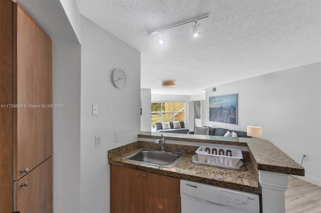 kitchen featuring rail lighting, sink, a textured ceiling, white dishwasher, and kitchen peninsula