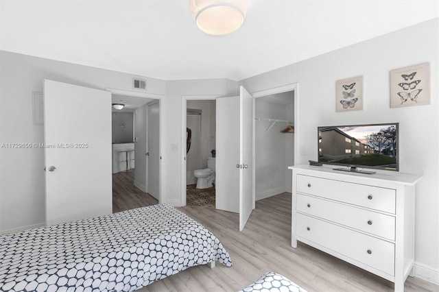 bedroom featuring a walk in closet, connected bathroom, light wood-type flooring, and a closet