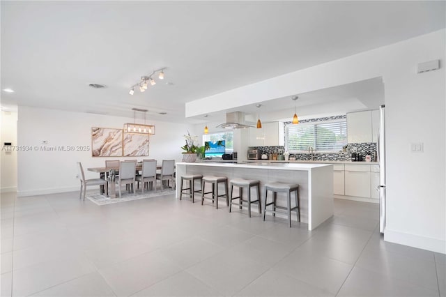 kitchen with pendant lighting, tasteful backsplash, white cabinetry, a kitchen bar, and a center island