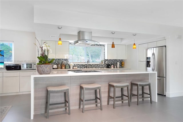 kitchen featuring stainless steel fridge with ice dispenser, hanging light fixtures, a kitchen breakfast bar, island exhaust hood, and white cabinets