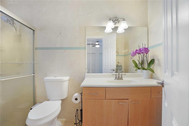 bathroom featuring vanity, toilet, a shower with door, and tile walls