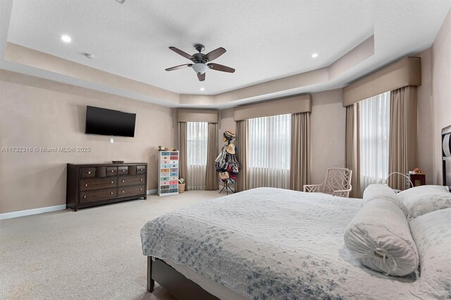 bedroom with a textured ceiling, a raised ceiling, ceiling fan, and carpet flooring