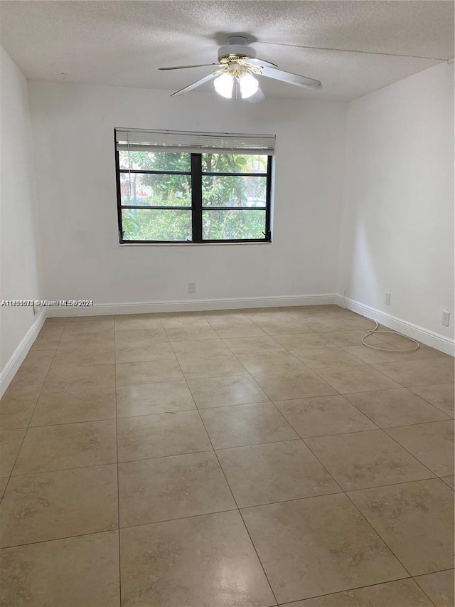 tiled empty room with ceiling fan and a textured ceiling