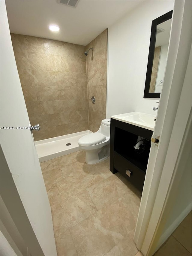 bathroom featuring vanity, a tile shower, and toilet