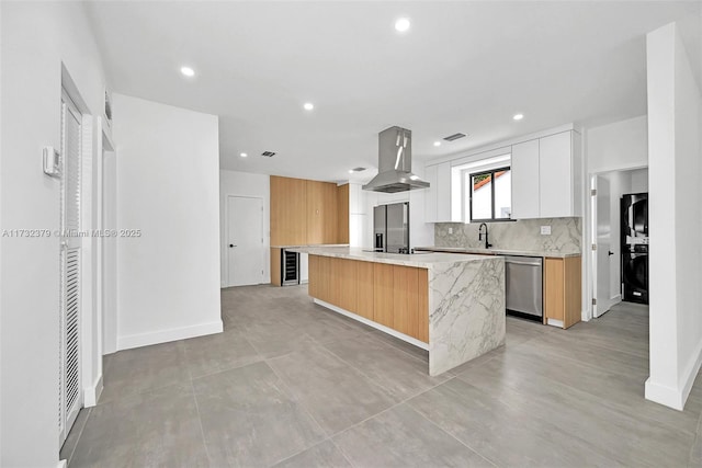 kitchen featuring stacked washer / dryer, white cabinetry, island exhaust hood, black appliances, and a center island with sink