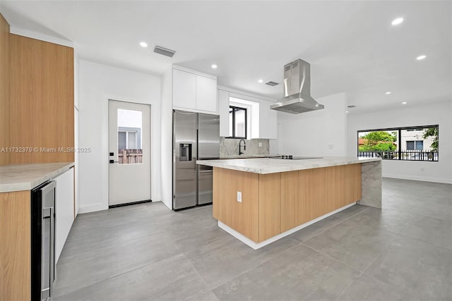 kitchen with sink, white cabinets, island exhaust hood, stainless steel fridge with ice dispenser, and light stone countertops