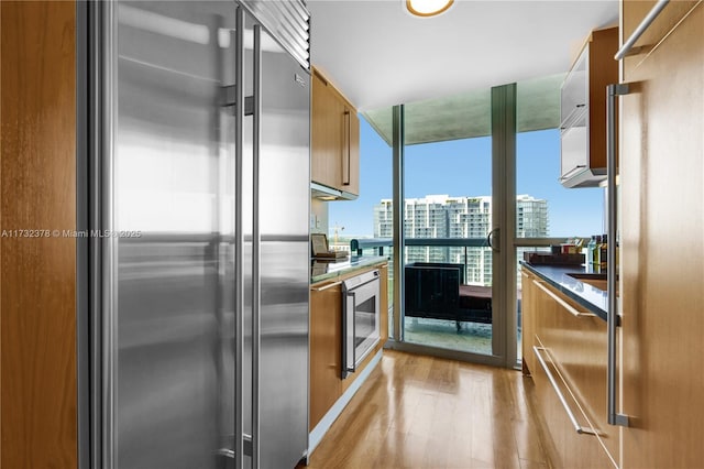 kitchen featuring high end fridge, wine cooler, floor to ceiling windows, and light wood-type flooring